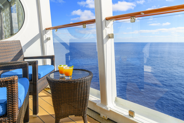 two tropical mixed alcohol drinks sit on a small end table on the balcony veranda of a cruise ship stateroom on a sunny day on the mediterranean sea.