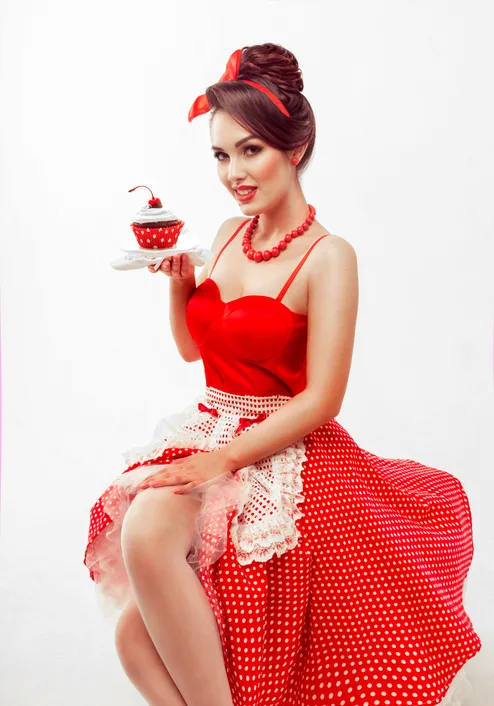 pin up housewife in a red dress with a delicious cake (dessert) beautiful young brunette woman on a white isolated background. studio photography